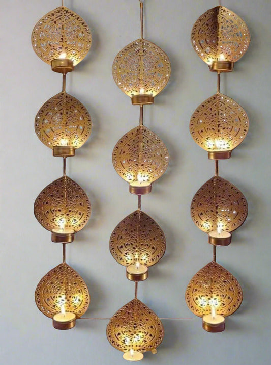A series of gold-colored iron tea light holders with intricate patterns, displaying multiple candles, set against a dark background with flower decorations.