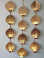 A series of gold-colored iron tea light holders with intricate patterns, displaying multiple candles, set against a dark background with flower decorations.